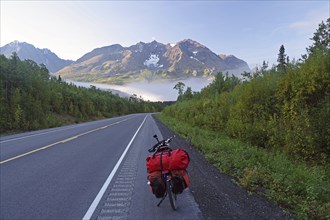 Bicycle on a straight, traffic-free road, fog, foliage colouring and snow-covered mountains,