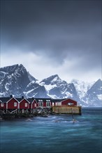 Rorbuer cabins of Hamnoy by the fjord, snowy mountains in the back, Hamnoy, Reine, Moskenesoya,