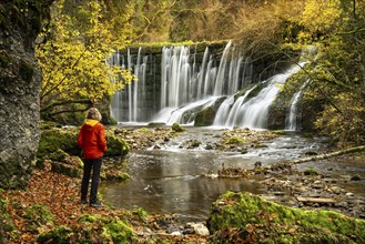 The Geratser waterfall in autumn. A hiker stands on the bank. Moss-covered rocks and trees in