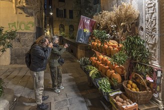 Tourists photographing a fruit shop in the evening in the historic centre, Genoa, Italy, Europe