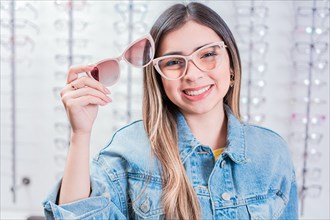 Smiling female customer trying on glasses in eye shop. Beautiful girl trying on glasses in an eye