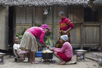 Malagasy family cooking maniok in front of traditional wooden house in rural village,