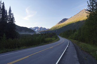 Traffic-free road leads as grades towards rugged mountains illuminated by the morning sun,