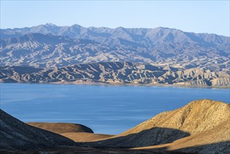 Blue Toktogul reservoir between dry mountain landscape, hilly mountains in the evening light,