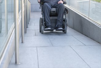 Man in a wheelchair using a ramp next to stairs