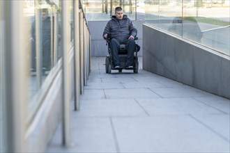 Man in a wheelchair using a ramp next to stairs