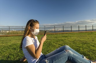 Young woman sitting on the grass with a protective mask during the SARS CoV-2 pandemic season