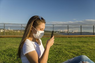 Young woman sitting on the grass with a protective mask during the SARS CoV-2 pandemic season