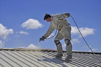 A trademan uses an airless spray to paint the roof of a building