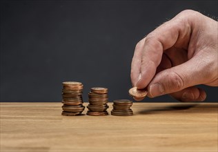 A hand stacking coins on a wooden table against a dark background