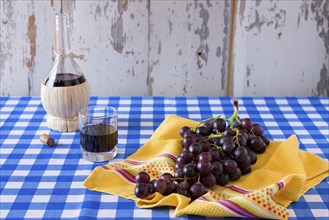 Bunch of red grapes and a glass of red wine with a wine flask on a checkered tablecloth