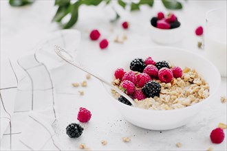 Morning healthy breakfast, white bowl full with granola, muesli, raspberry, blackberry on gray