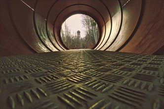 View through a metal pipe. In the background between trees is a water tower. Art with rare angle