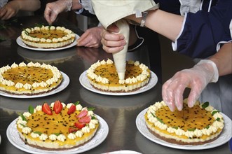 Cook placing cream on the top of a passionfruit cheesecake