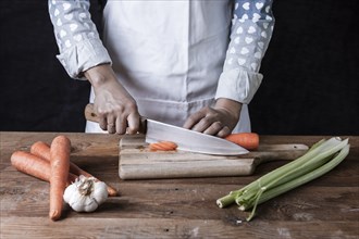 Cutting carrots on a cutting board with celery and garlic on the table