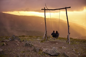 Romantic couple social distancing swinging on a Swing baloico in Lousa mountain, Portugal at sunset