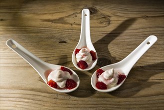 Mascarpone cream and strawberries on ceramic spoons over a wooden background