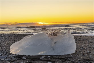 An iceberg with the sun in the background at sunrise on Diamond Beach next to Jokulsarlon in winter