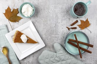 A flat lay concept photo with space for text of pumpkin pie, whiped cream, cinnamon sticks, and