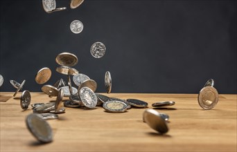 Different coins falling on a wooden table against a dark background