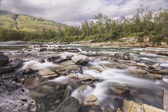 Abiskojakka, river in Abisko NP (northern Sweden) . Long exposure, rocks, birch, clouds, grey sky,