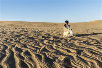 A woman dressed in white is watching the sunset on a dune