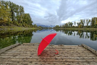 A concept photo of a red umbrella resting on a wooden dock by Kootenai RIver in north Idaho during