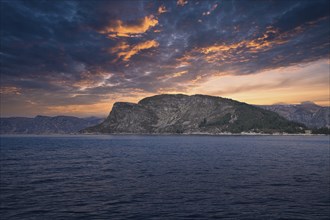 Westcap in Norway. Mountain that reaches into the fjord. Cloudy sky with clouds illuminated by the