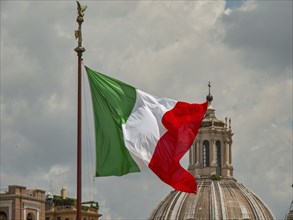 The Italian flag flies dynamically in front of a dome under a cloudy sky, rome, italy
