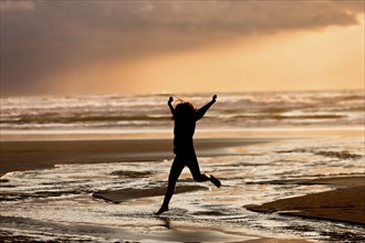 A girl in silhouette at sunset leaps into the creek on Nye Beach that flows into the ocean in