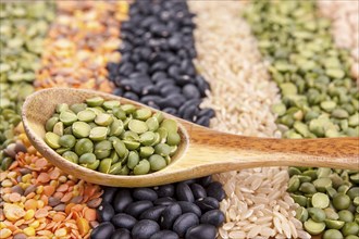 Neatly laid out rows of assorted dried grains and a wooden spoon with split peas in it