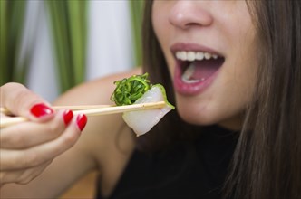 Woman eating delicious gunkan sushi, closeup on chopsticks