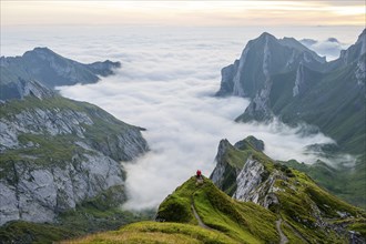 Two hikers enjoying the view over the Säntis mountains into the valley of Meglisalp at sunrise,