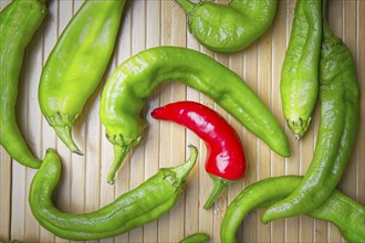 A flat lay photo of long green peppers and a shorter red pepper displayed on a mat