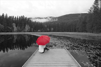 A concept photo of a black and white image with a woman holding a red umbrella while sitting on a