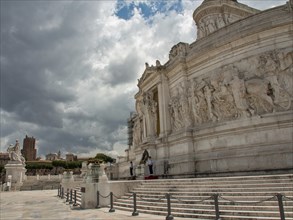 Side view of a massive monument with reliefs and steps under a dramatic sky, rome, italy