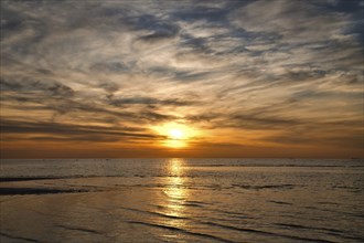 Sunset, illuminated sea. Sandy beach in the foreground. Light waves. Poel island on the Baltic Sea.