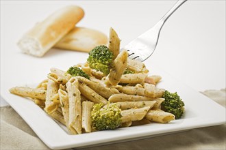 A still life photo of a plate of pesto pasta and a fork with pasta and broccoli on it