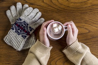 Overview shot of hands holding a hot cup of cocoa and a pair of gloves