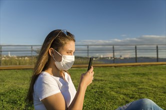 Young woman sitting on the grass with a protective mask during the SARS CoV-2 pandemic season