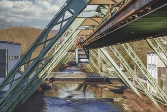 A suspension railway runs on an elevated bridge over a river, the scene is complemented by a clear