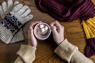 Overview shot of hands holding a hot cup of cocoa by gloves and a scarf