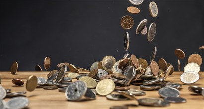 Different coins falling on a wooden table against a dark background