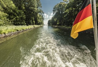 Drive shaft of a boat passing through a canal with a waving German flag