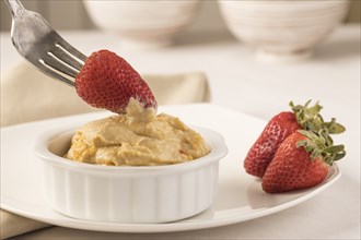 A close up photo of a strawberry being dipped into a bowl of hummus