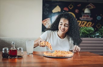 Happy afro hair woman eating pizza in a restaurant. Lifestyle of afro-haired woman enjoying a pizza