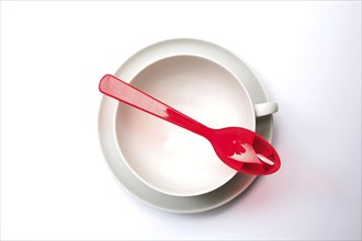 Crockery and cutlery, empty teacup with saucer, seen from above, a red plastic spoon lies on it