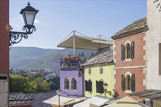 Tourists on terrace of restaurant and pastel coloured houses in the Old Town of Mostar,