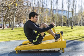 Confident young man doing abdominal exercises on a public equipment in outdoor fitness