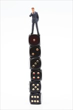 Symbol photo, man (figure) standing perplexed on a stack of dice showing the values 1 to 6 in